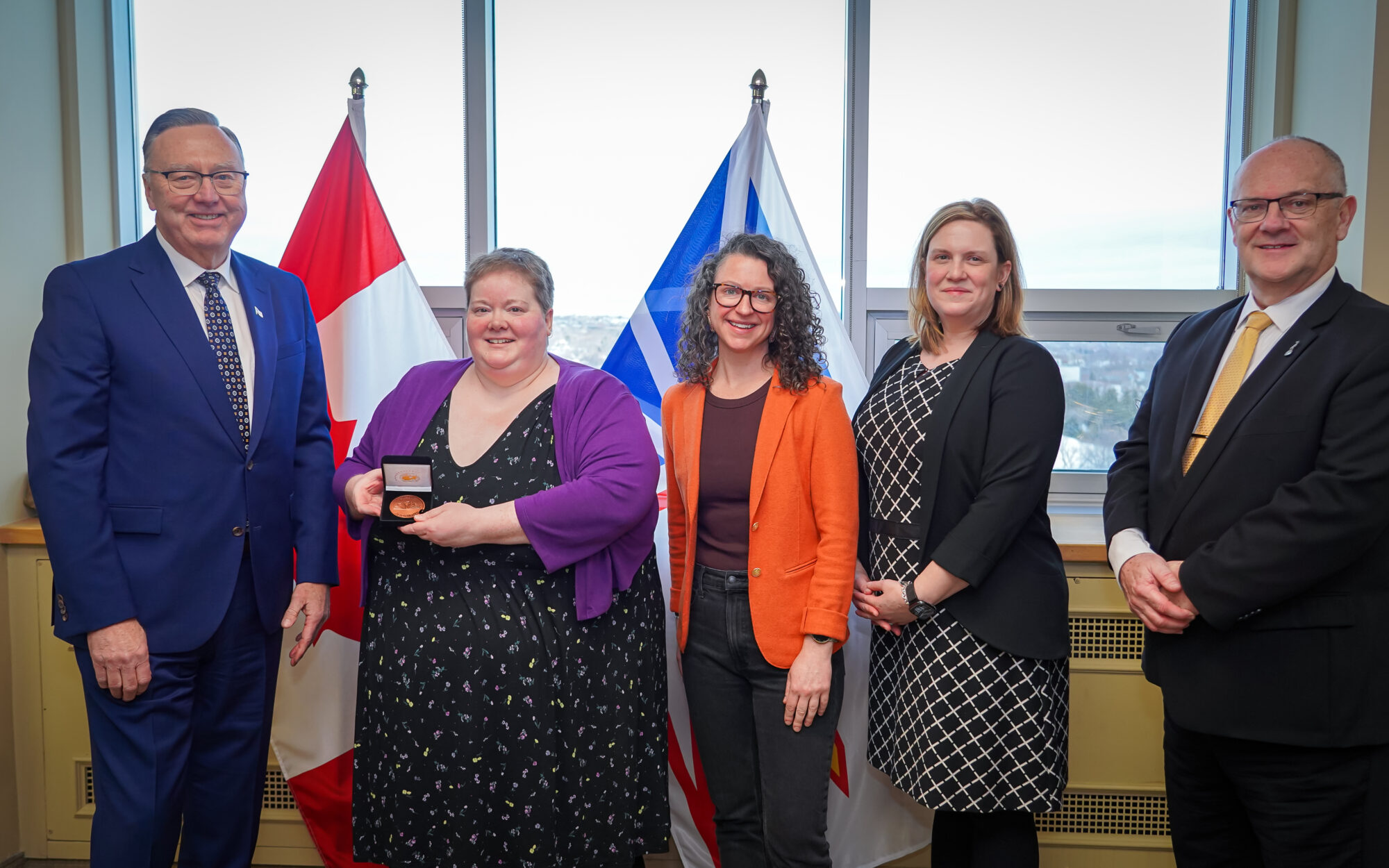 Representatives of Stella’s Circle stand with officials in front of provincial and national flags as an award medal is presented during a literacy award recognition event.